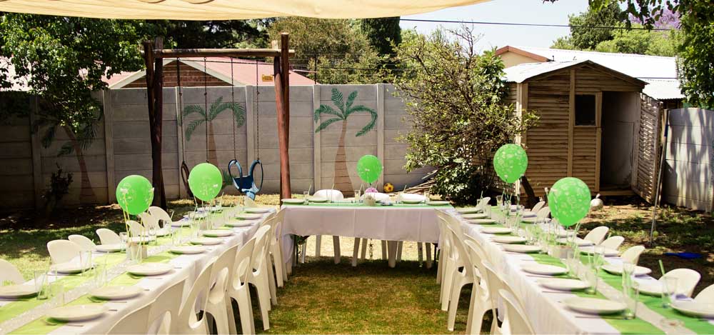 long tables, place settings, chairs, and balloons set up in a backyard