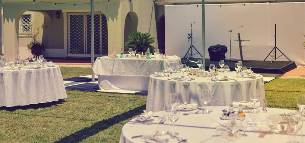 round tables, place settings, chairs and a stage set up outside for a wedding